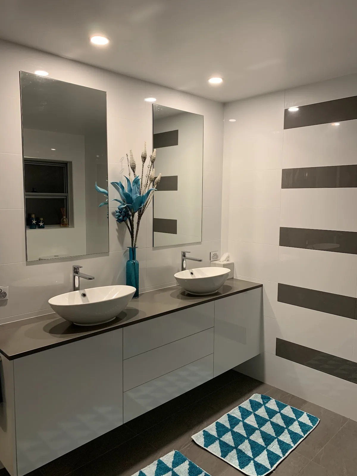 Double vanity with vessel basins lit by downlights in a white bathroom