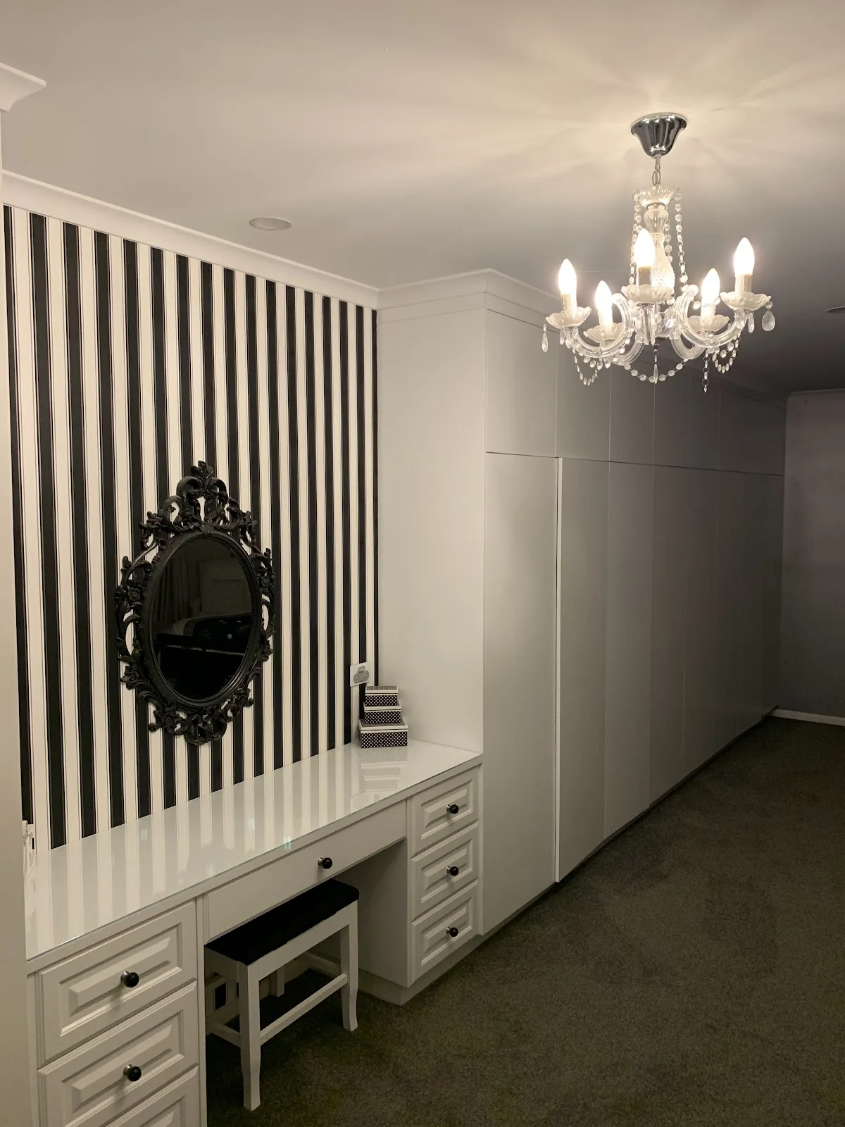 Crystal chandelier over a dressing room with a striped feature wall