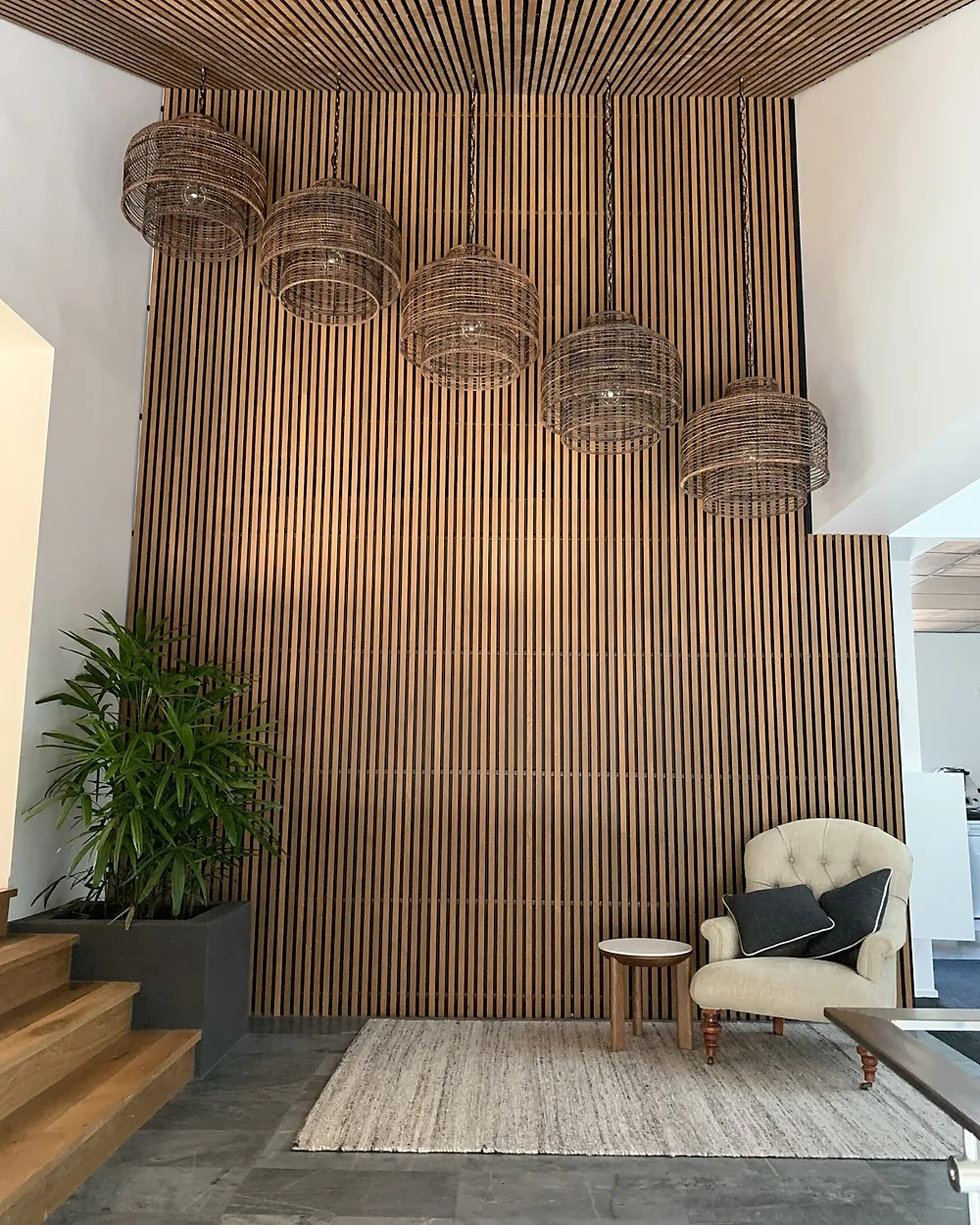 Row of woven pendant lights hanging in front of a tall timber batten feature wall