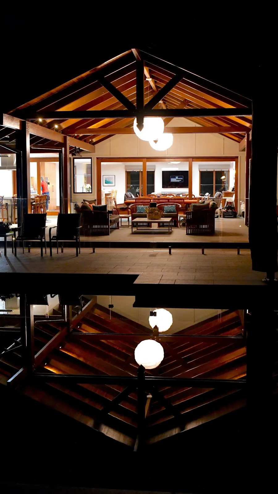 Timber pavilion lit up at night with pendant globes and downlights, reflected in the pool