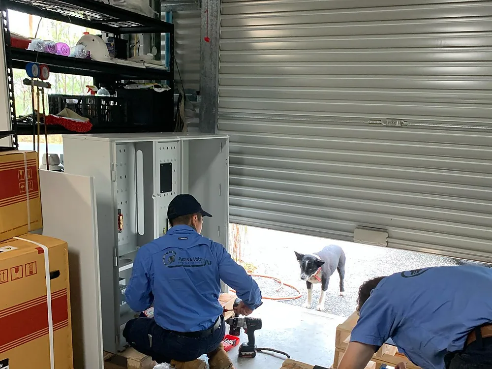 Two Watts & Volts electricians in branded shirts building a new switchboard enclosure in a shed