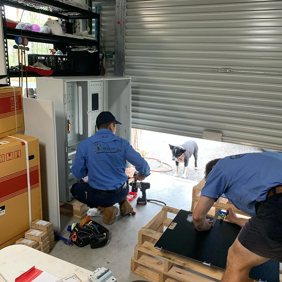 Electrician fitting out a new switchboard enclosure while a second electrician works on a panel