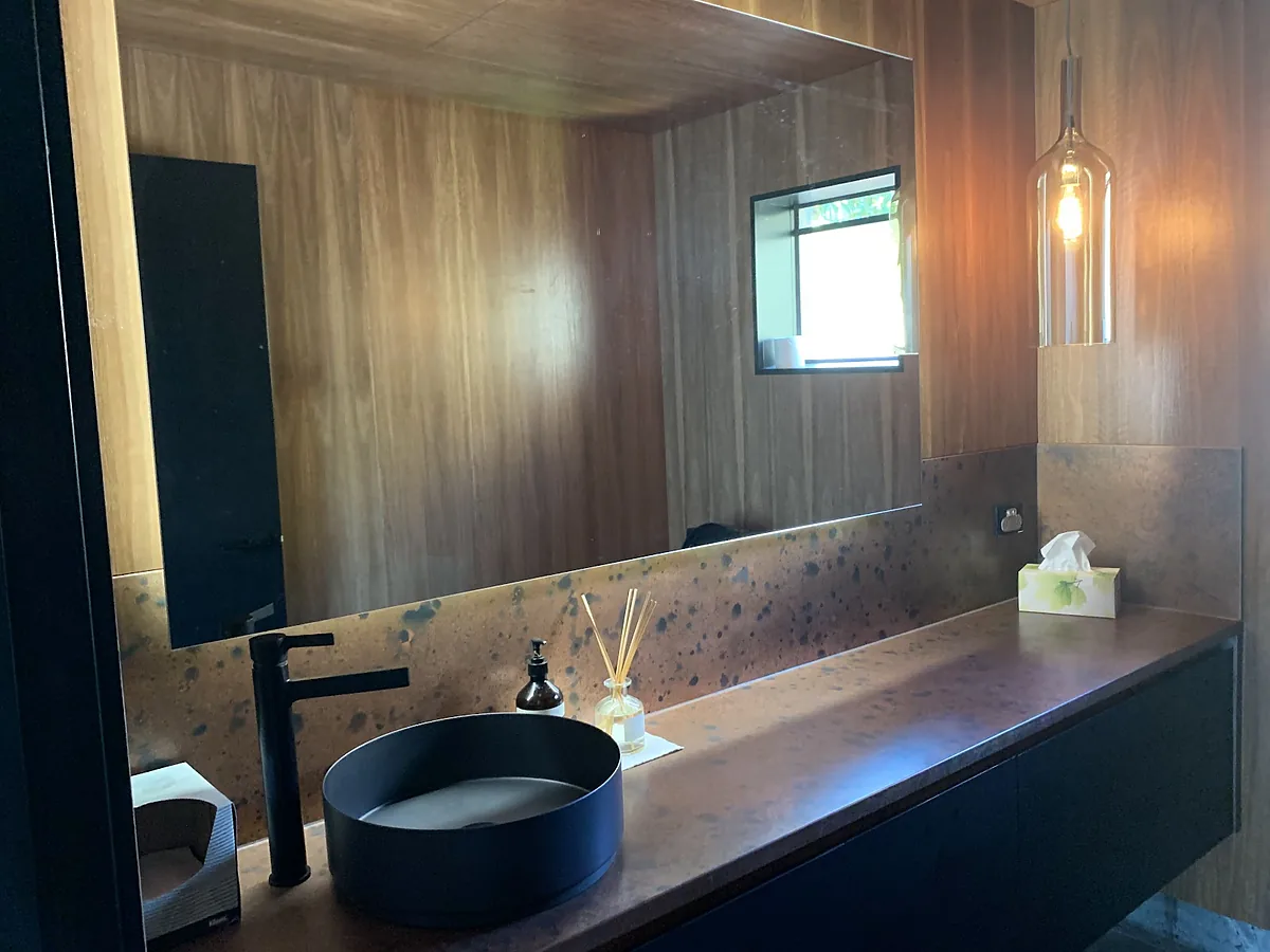 Timber-lined bathroom with a glass pendant light and backlit mirror above a dark vanity
